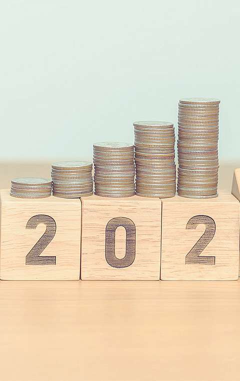 Sanduhr steht neben Holzblöcken. Auf den Holzblöcken sind Münzen gestapelt.