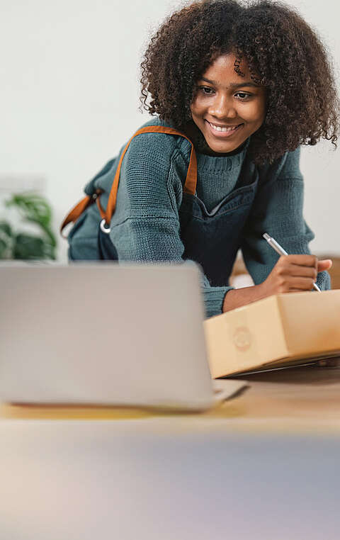  Frau schreibt etwas auf einen Karton und hat einen Laptop vor sich 