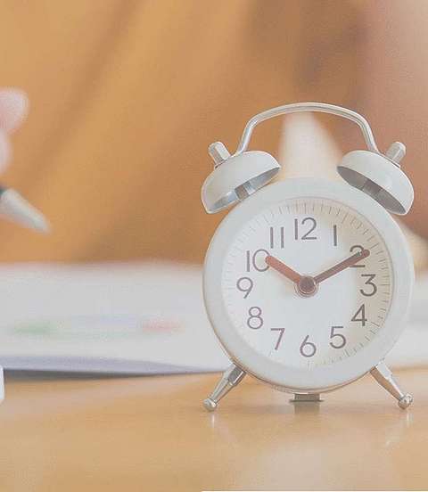  Eine Person sitzt an einem Tisch und notiert sich etwas, vor ihr steht ein kleiner weißer Wecker. 