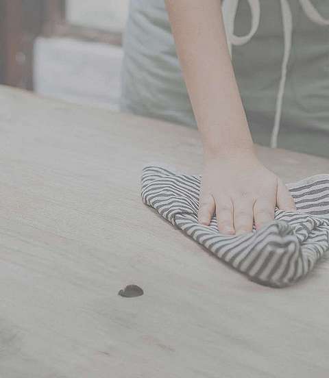 Person putzt mit einem Lappen einen Tisch