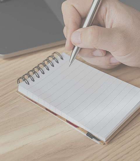 Person hält einen Kulli in der Hand und schreibt auf einen Notizblock