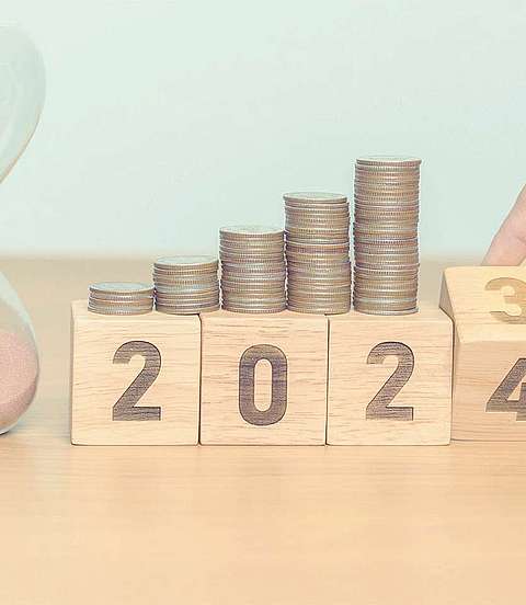 Sanduhr steht neben Holzblöcken. Auf den Holzblöcken sind Münzen gestapelt.