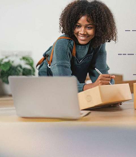  Frau schreibt etwas auf einen Karton und hat einen Laptop vor sich 