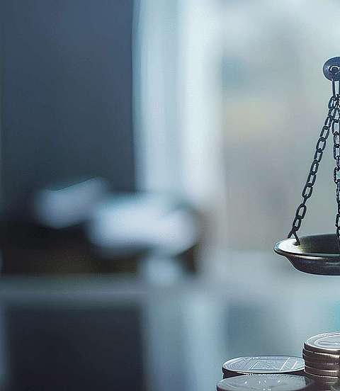 Vor einer silbernen Waage sind Münzen gestapelt